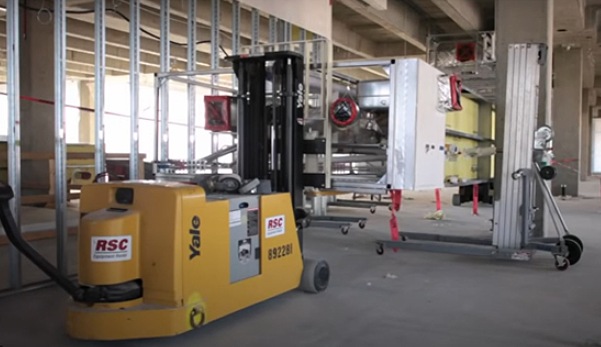 An electric pallet jack positioning a prefabricated MEP rack inside a construction building, demonstrating modern installation techniques.